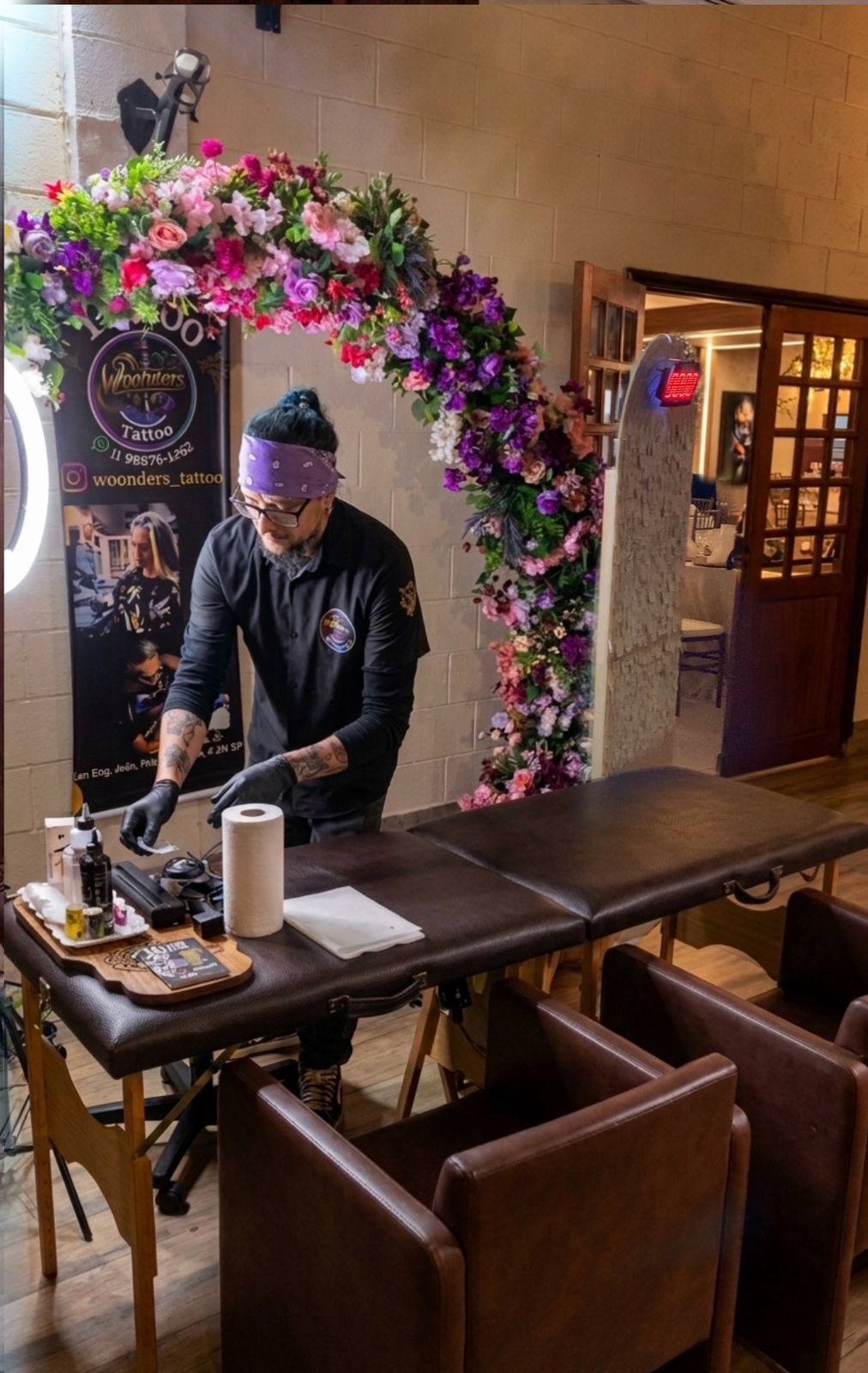 Tatuador Woonders preparando setup com arco floral